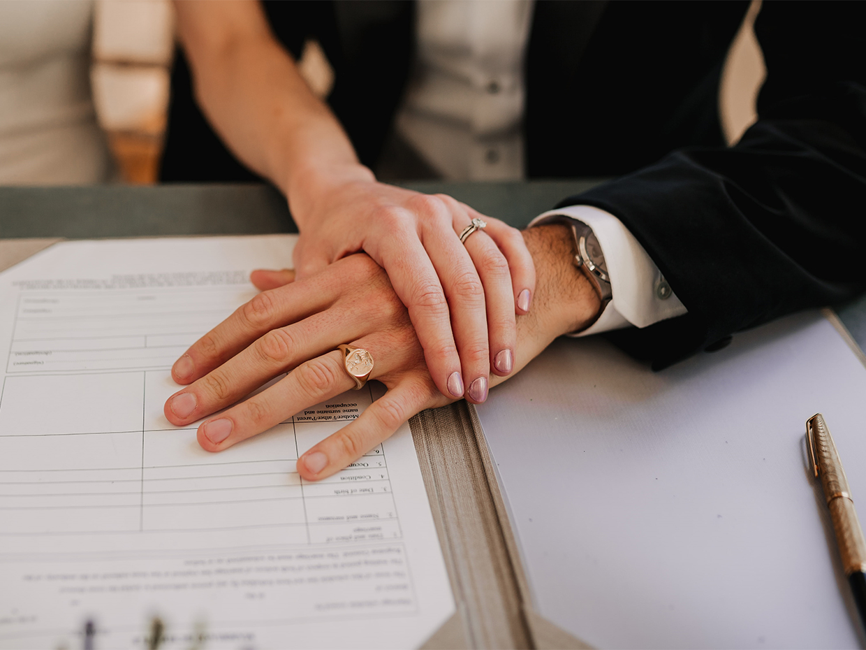 Newlywed couple with hands crossed on register with husband wearing engraved signet ring